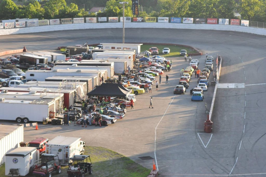 Early evening at the racetrack: teams and drivers prepare their vehicles in the bustling pit area, gearing up for a night of high-speed competition